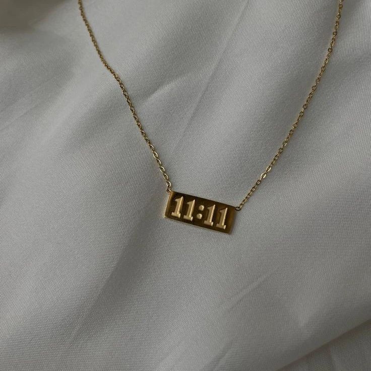 Gold necklace with '11:11' pendant on a light gray fabric background