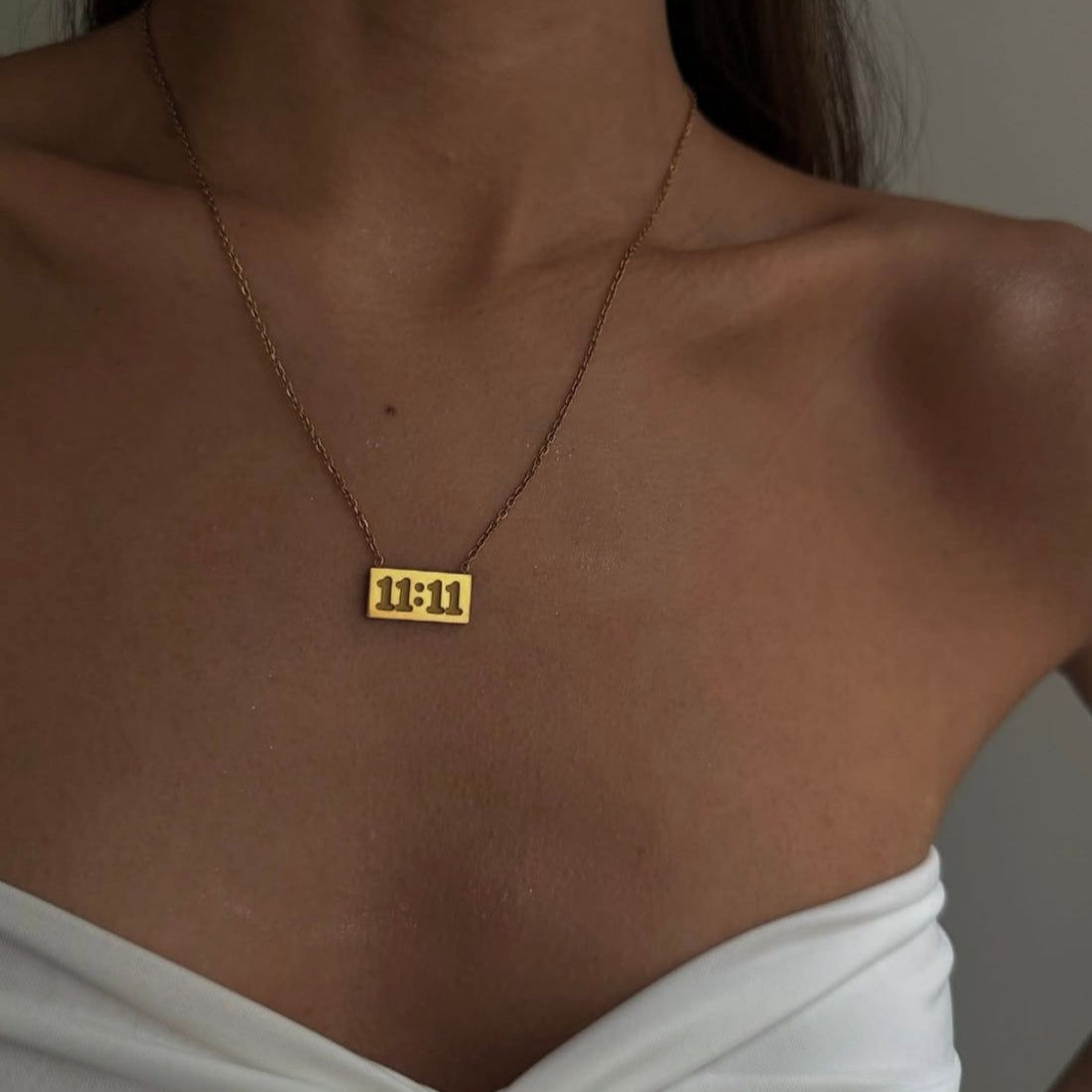 Gold necklace with a pendant on a person wearing a white top.