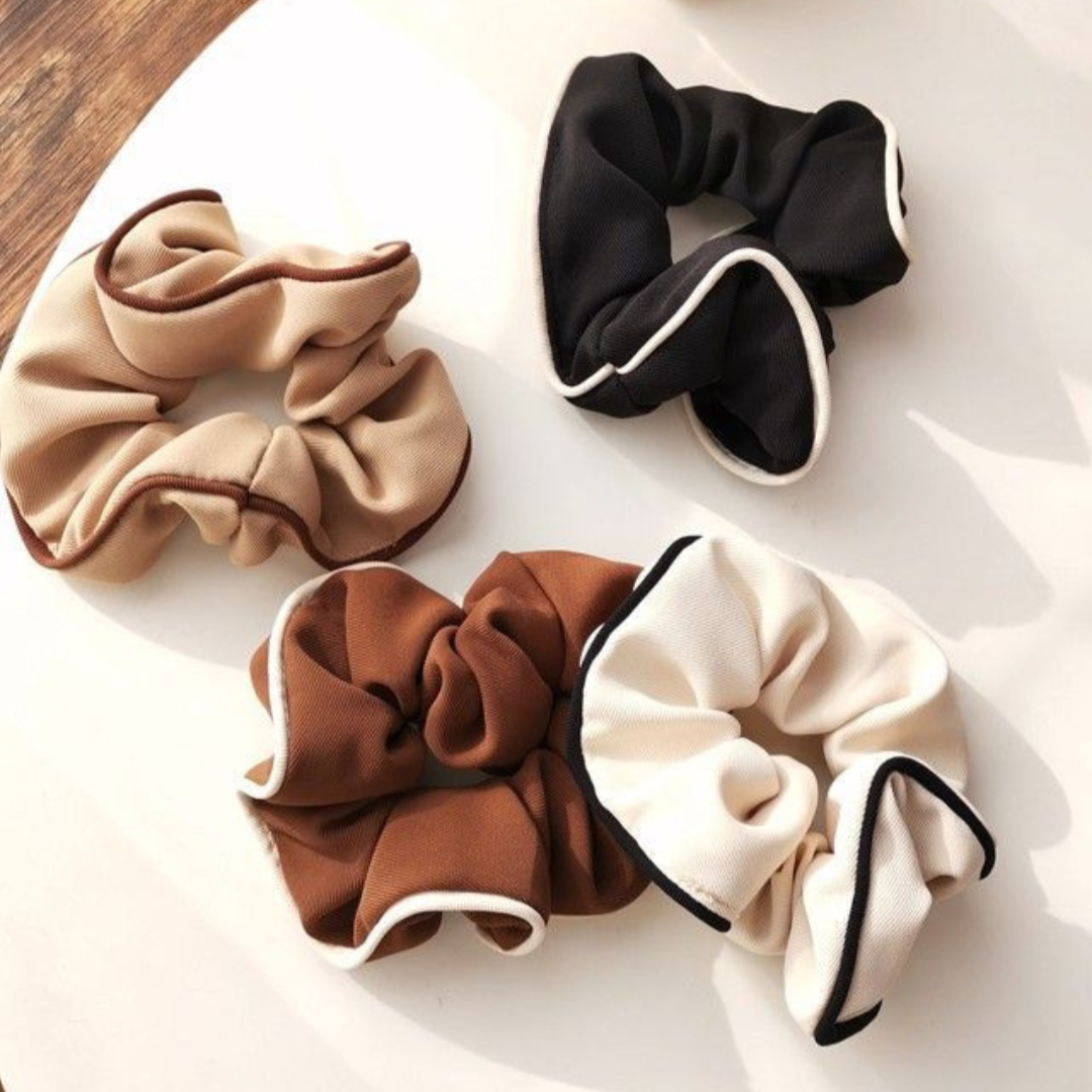 Four scrunchies in beige, brown, black, and white on a light surface.