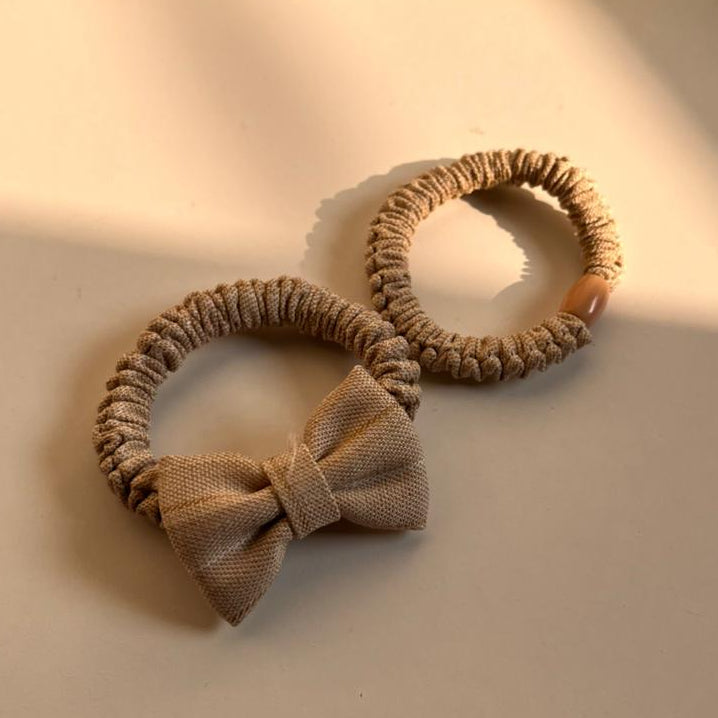 Two beige hair ties with a bow on a light surface with a soft focus background