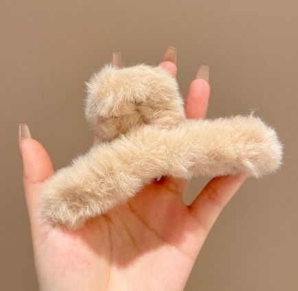 Beige fuzzy hair clip held in a hand against a beige background