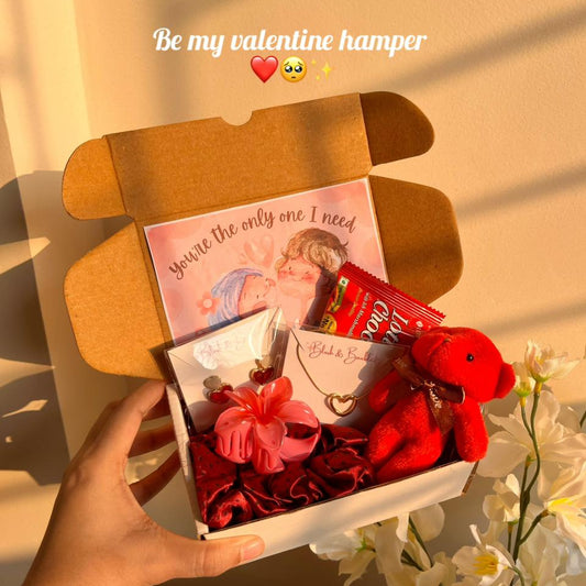 Valentine's Day hamper with a teddy bear, cards, and other items on a soft background.