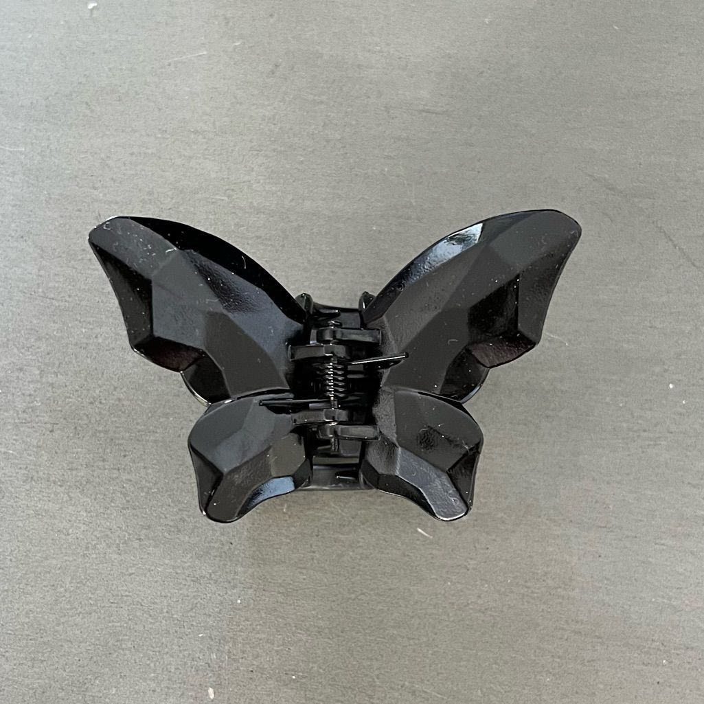 Black butterfly-shaped hair clip on a grey background