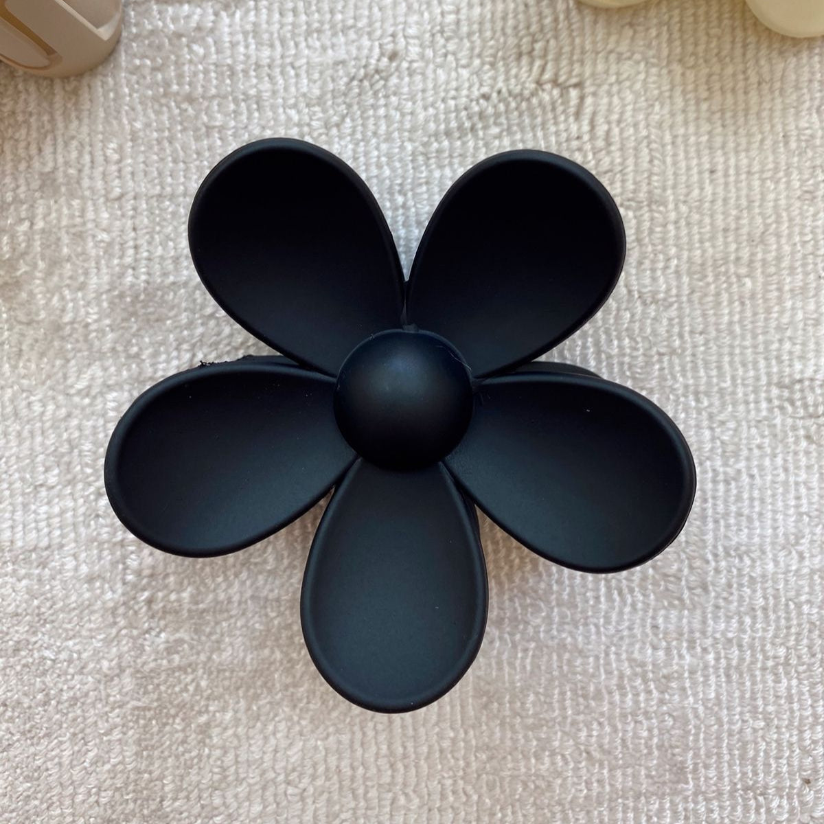 Black flower-shaped Hair claw clip on a textured beige surface