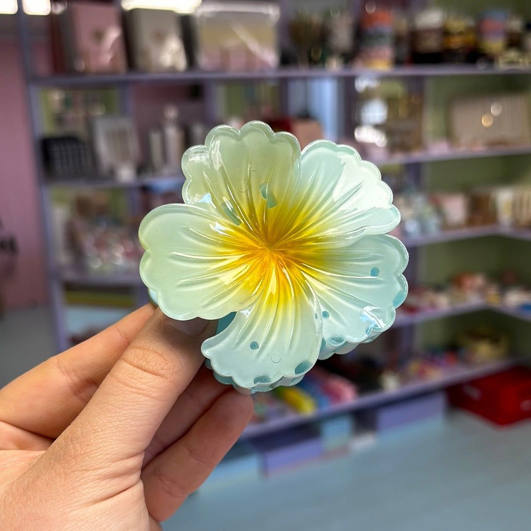 Hand holding a light green flower-shaped hair claw clip with a blurred indoor background