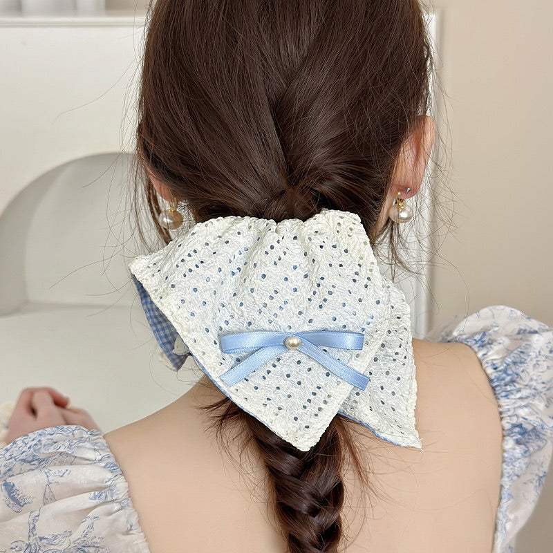 Woman with braided hair wearing a decorative hair accessory or a square shaped scrunchie with a blue ribbon.
