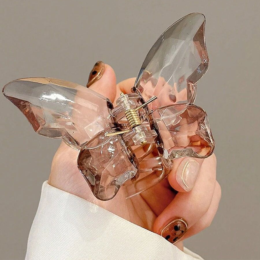 Clear butterfly-shaped hair clip held in a hand against a neutral background