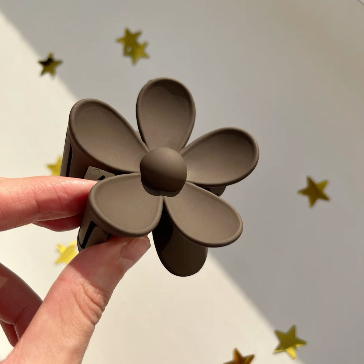 Brown flower-shaped hair clip held by a hand with gold stars on a light grey background