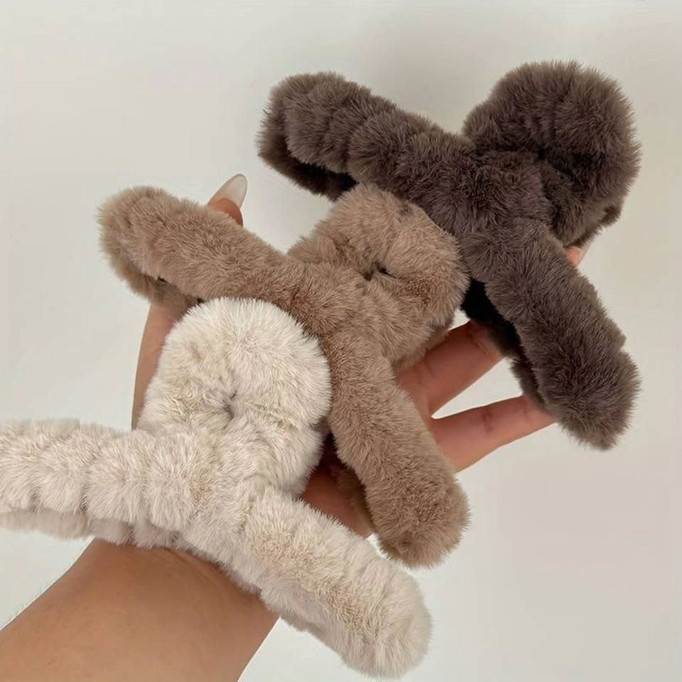 Two fluffy bunny-shaped hair ties held by a hand against a plain background