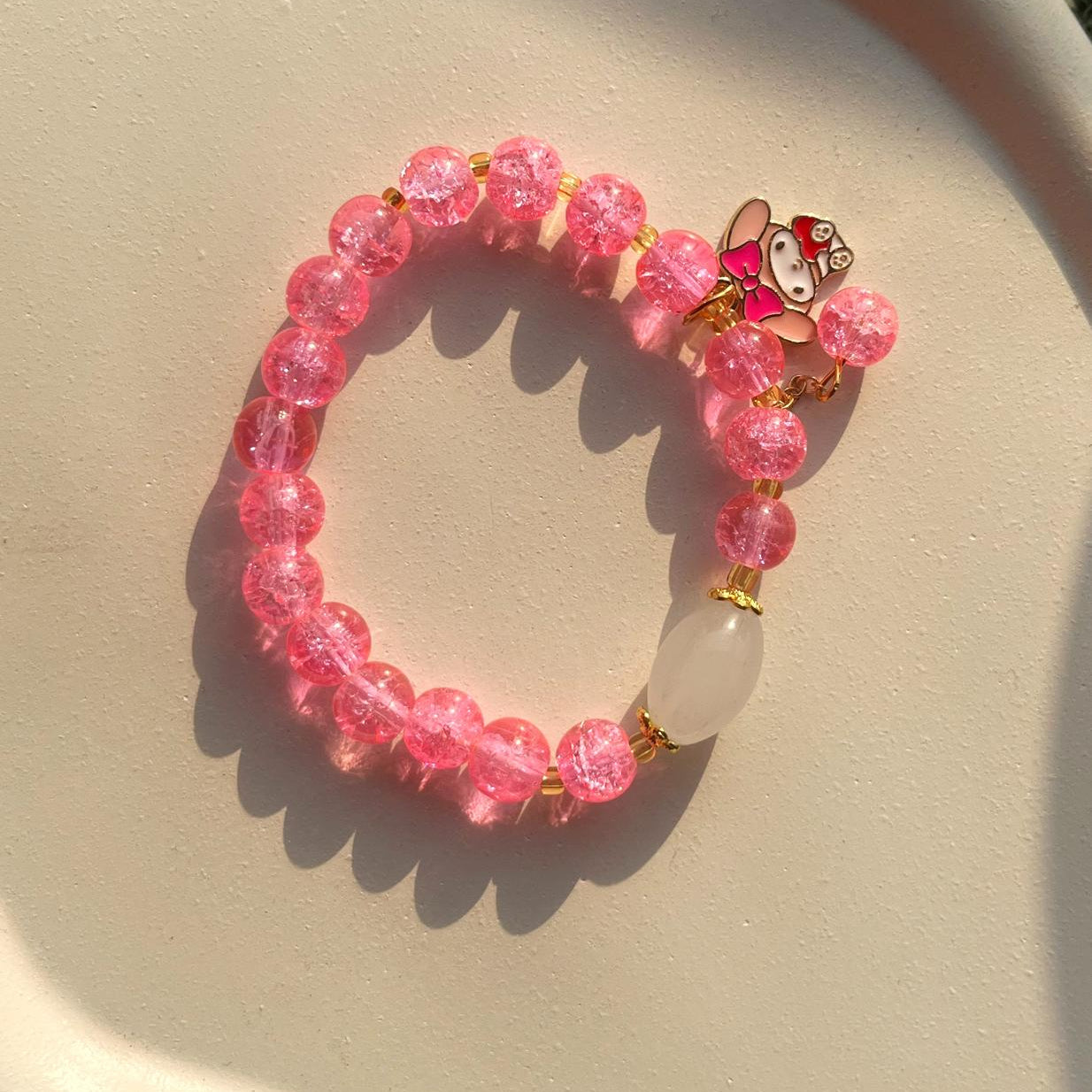Pink beaded bracelet with a small character charm on a beige surface