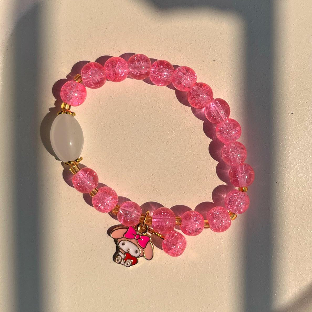 Pink beaded bracelet with a small charm on a light background