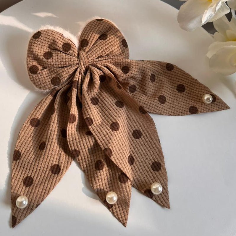 Brown polka dot bow with pearls on a white surface with flowers in the background