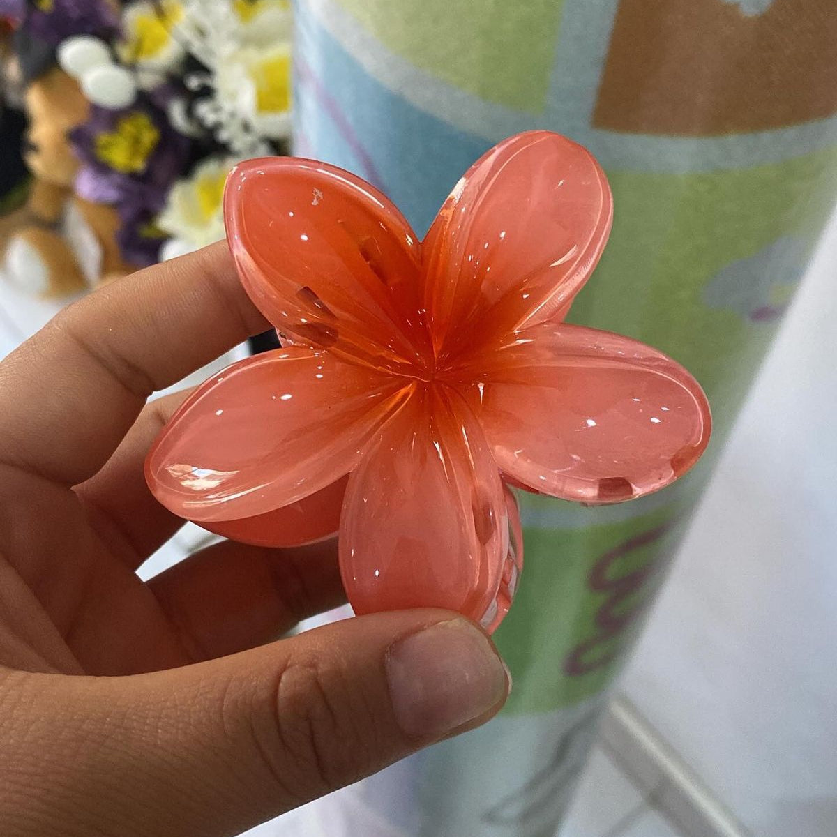 Hand holding a transparent orange flower-shaped viral claw clip with a blurred background