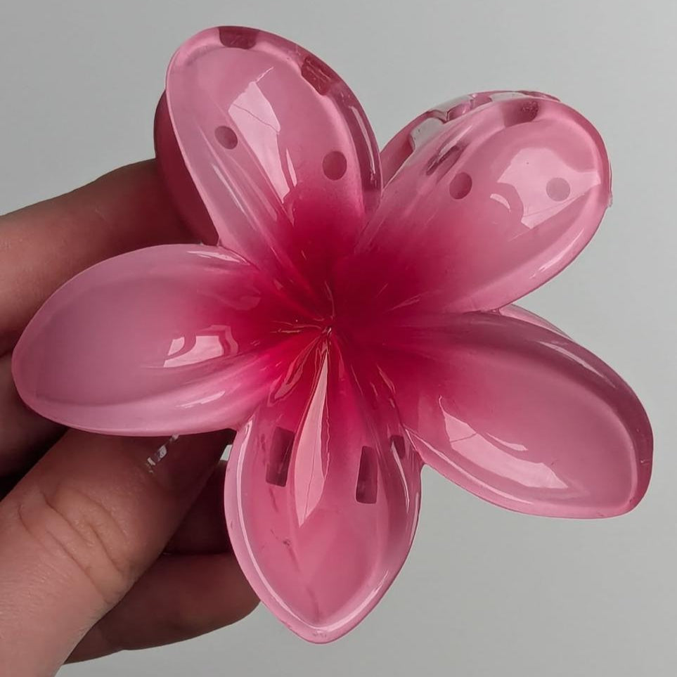Pink flower-shaped viral claw clip held by a hand against a gray background