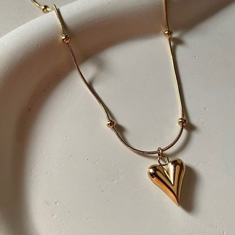 Gold necklace with a heart-shaped pendant on a light background