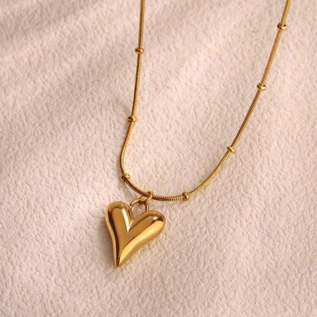 Gold heart-shaped pendant necklace on a light pink background