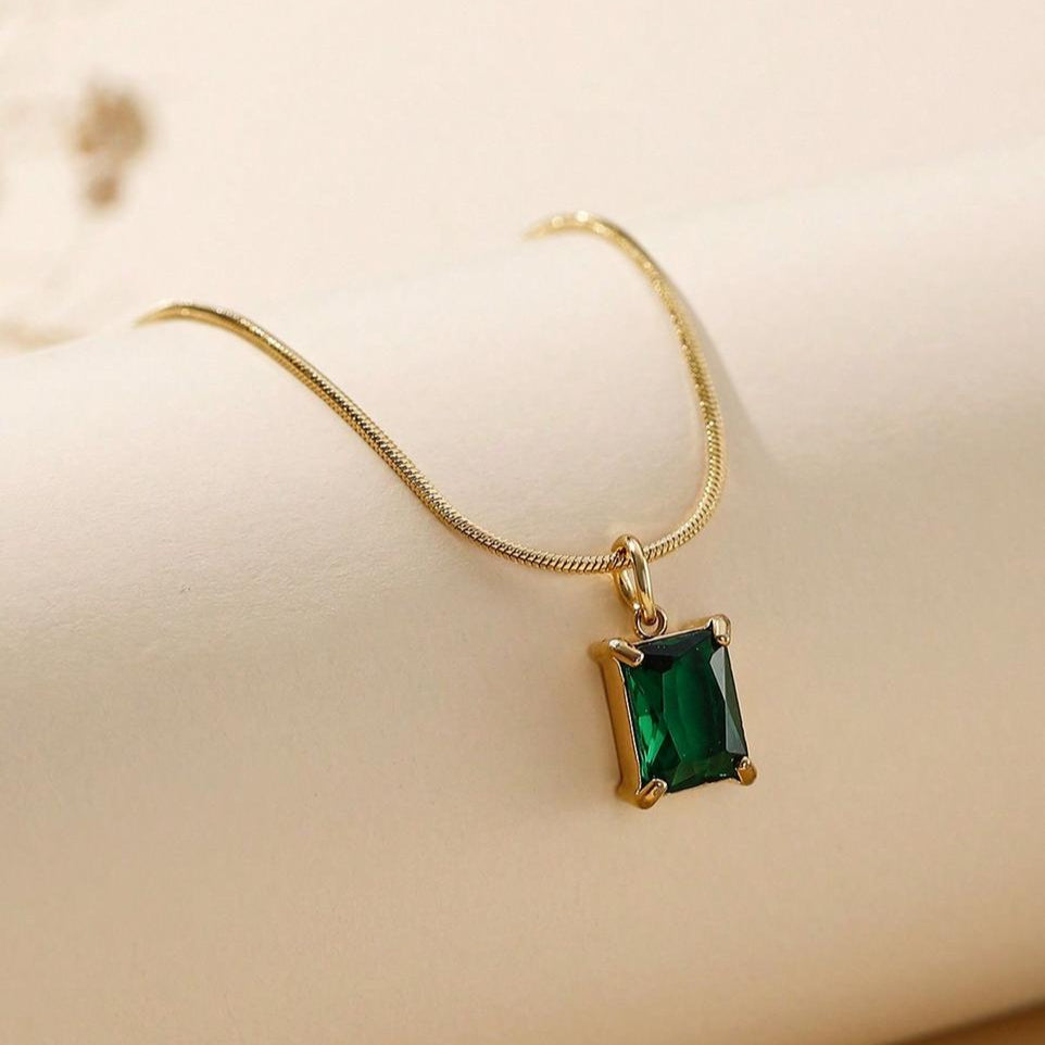 Gold necklace with a green gemstone pendant on a beige background