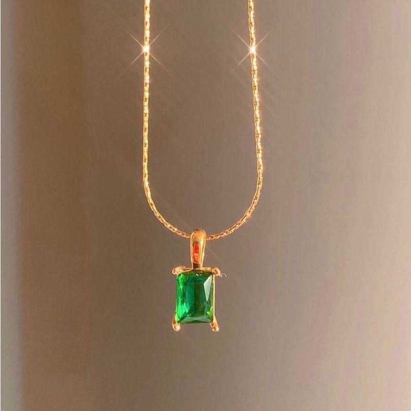 Gold necklace with a green gemstone pendant on a gray background