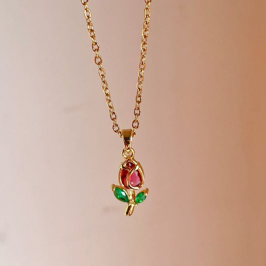 Gold necklace with a pendant featuring a red gemstone and green accents on a blurred background