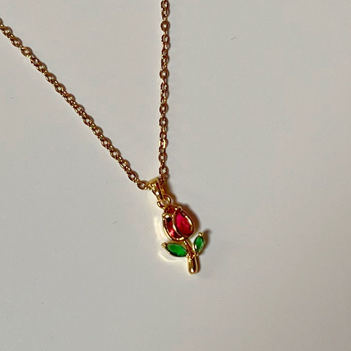 Gold necklace with a red gemstone pendant on a light gray background