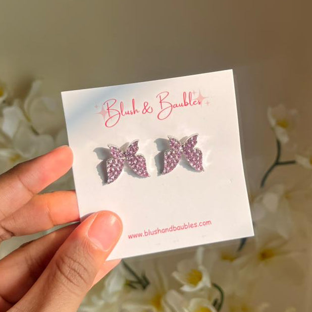 Butterfly earrings on a card held by a hand with flowers in the background