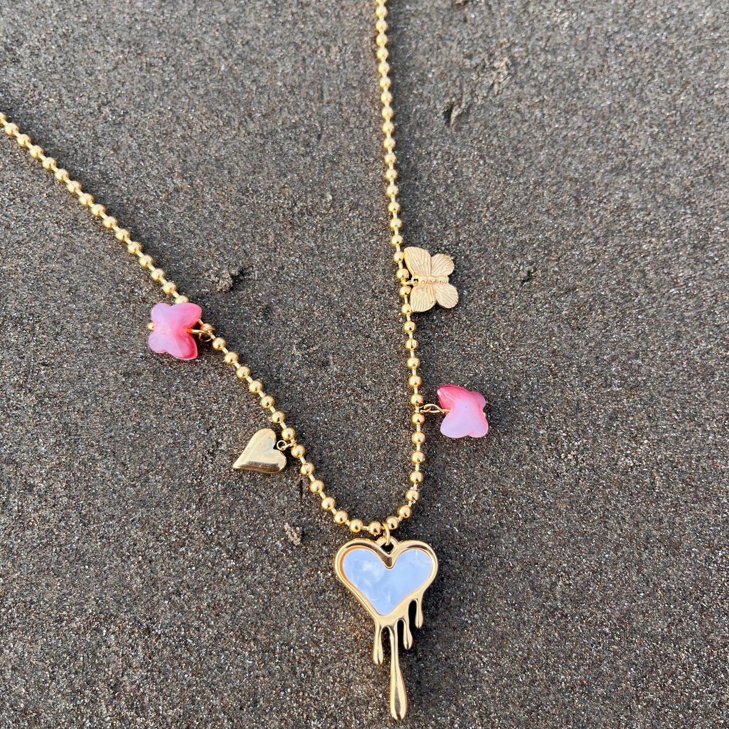 Necklace with heart and clover pendants on a sandy surface
