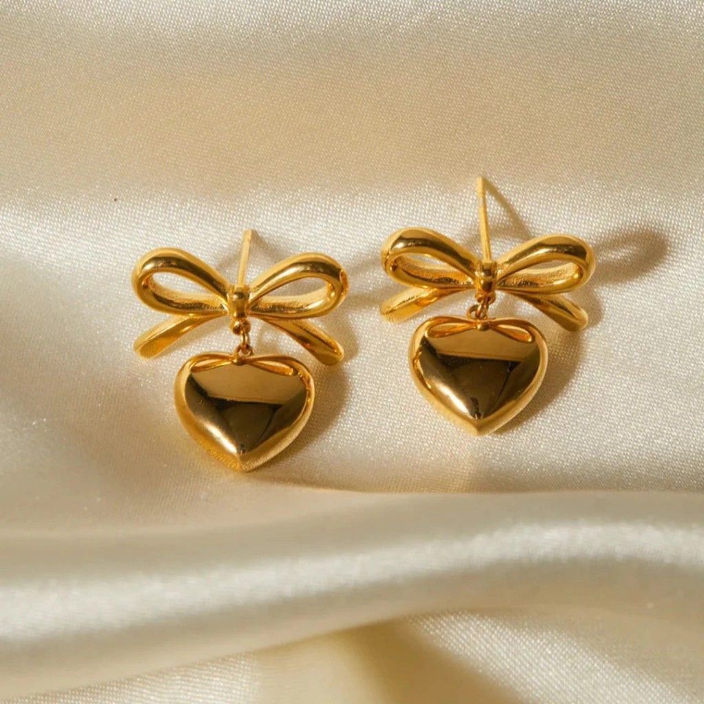 Gold bow-shaped earrings on a beige fabric background