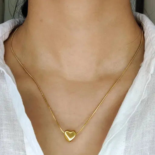 Gold heart-shaped necklace worn by a person with a white shirt.