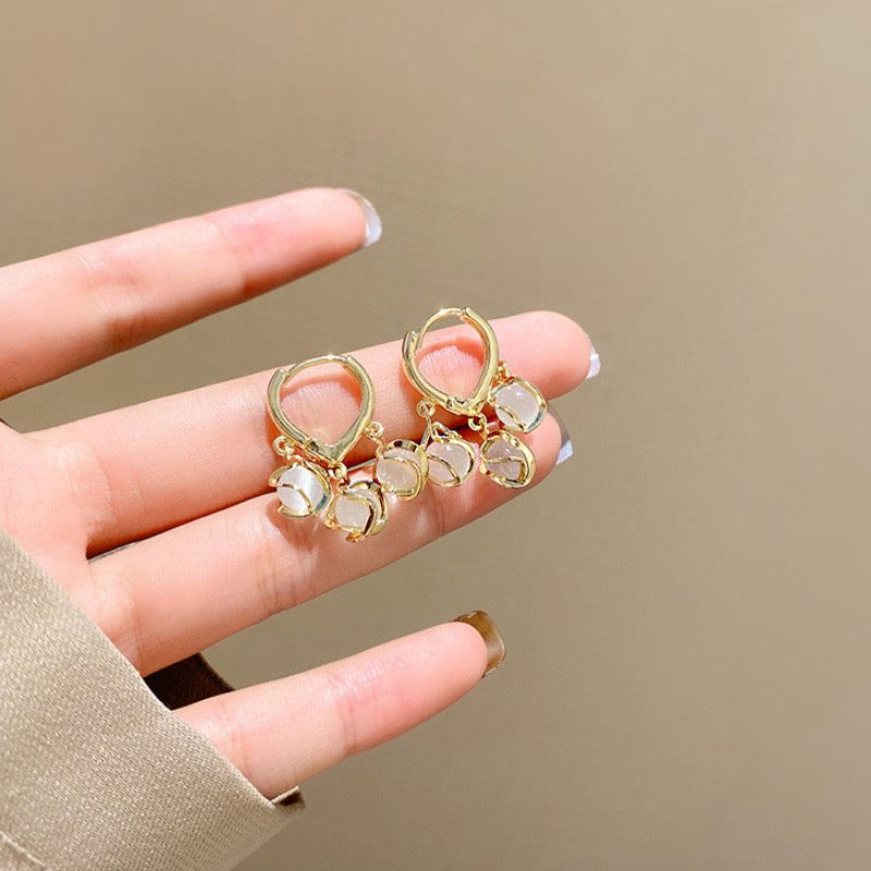 Gold earrings with clear stones held between fingers against a beige background