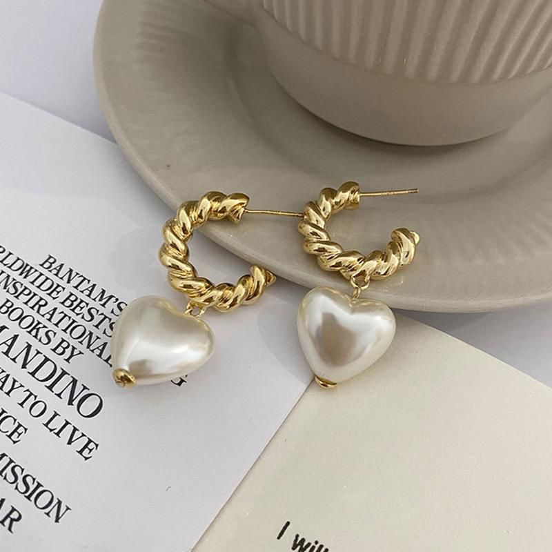 Gold hoop earrings with heart-shaped pearls on a book and saucer background