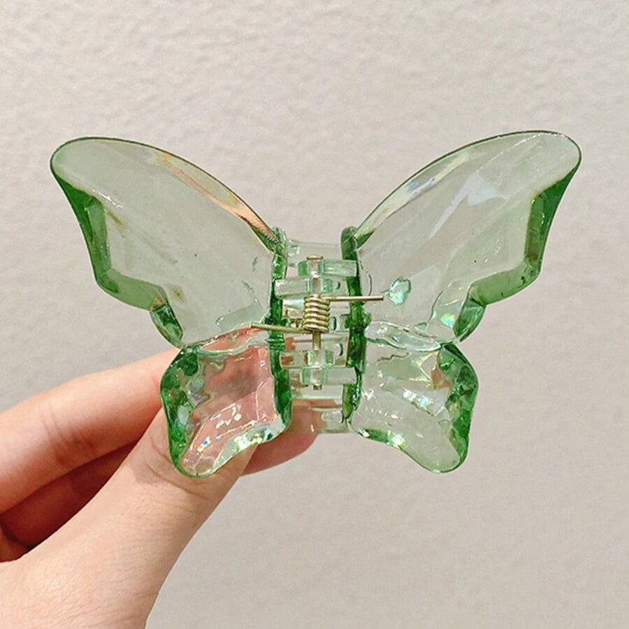 Green butterfly hair clip held by a hand against a neutral background
