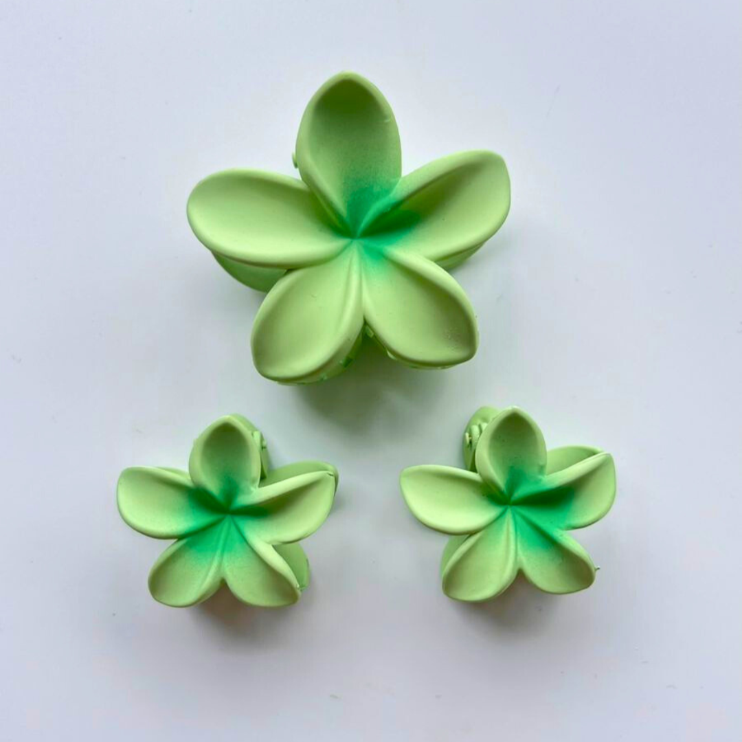 Three green flower-shaped hair claw clips on a white background.