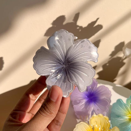 Hand holding a floral-shaped hair clip with colorful flowers in the background