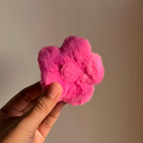 Hand holding a pink fuzzy hair clip against a plain background