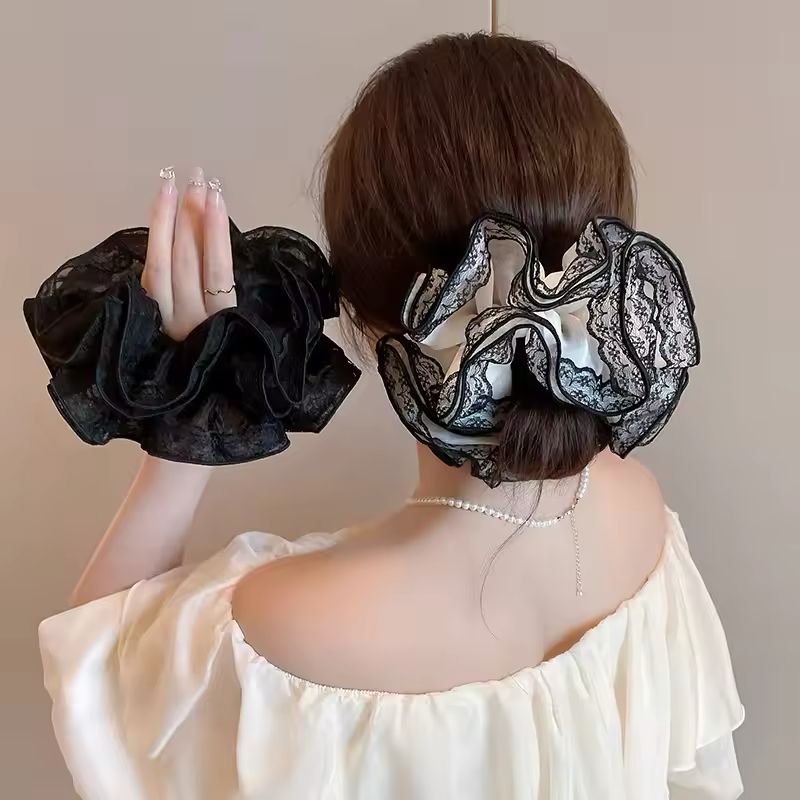 Person wearing black lace scrunchies on a plain background