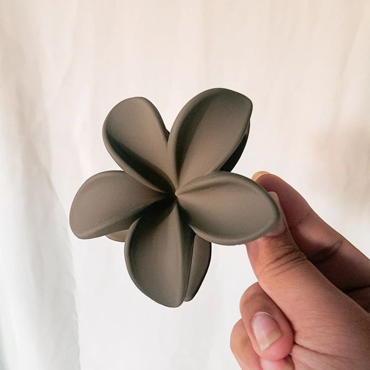 Hand holding a gray flower-shaped hair clip against a plain background