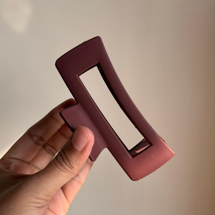 Hand holding a maroon rectangular hair clip against a neutral background