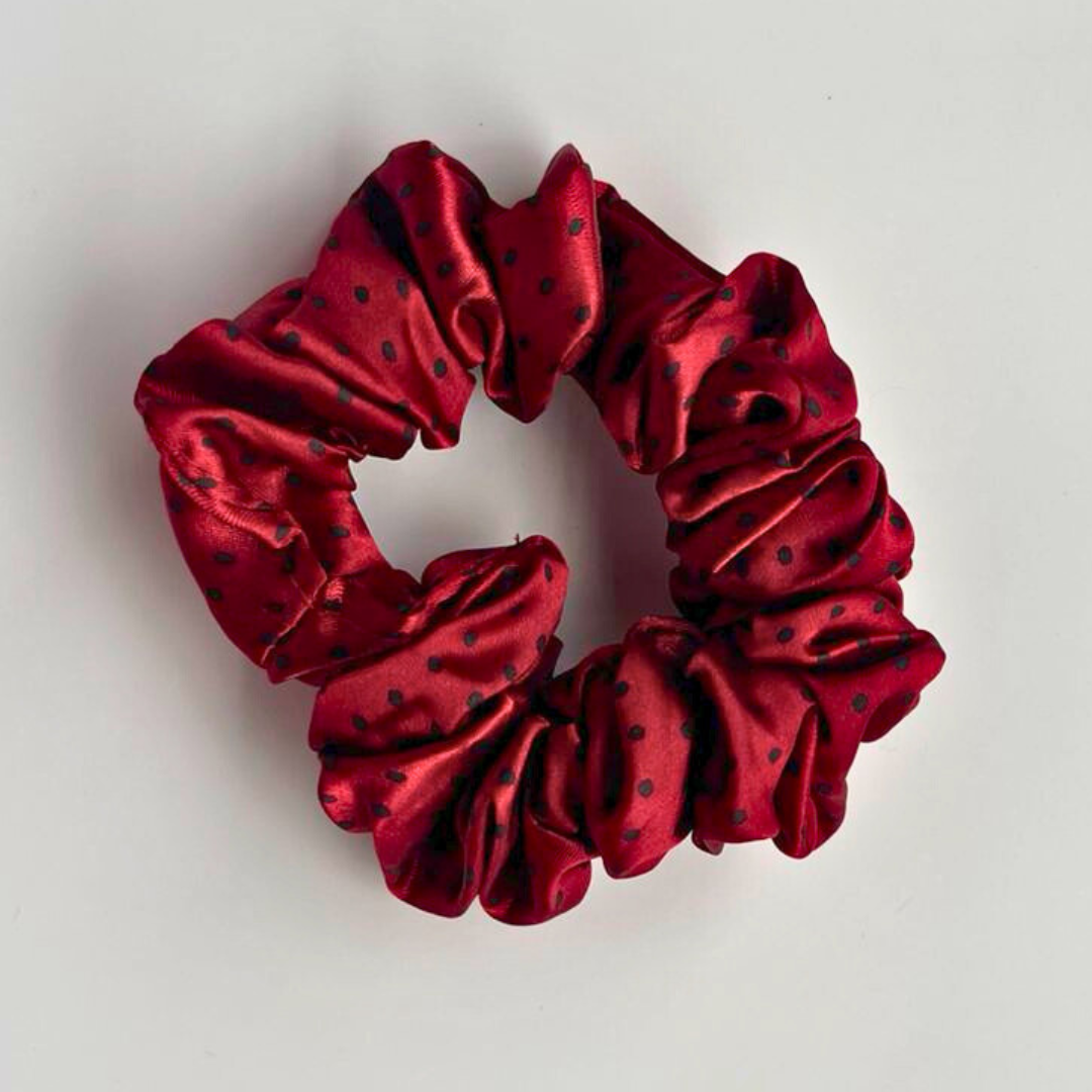 Red satin scrunchie with black polka dots on a light gray background