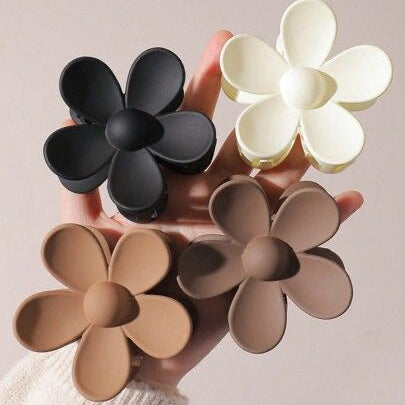 Flower-shaped hair claw clips in black, white, and beige held by a hand against a neutral background