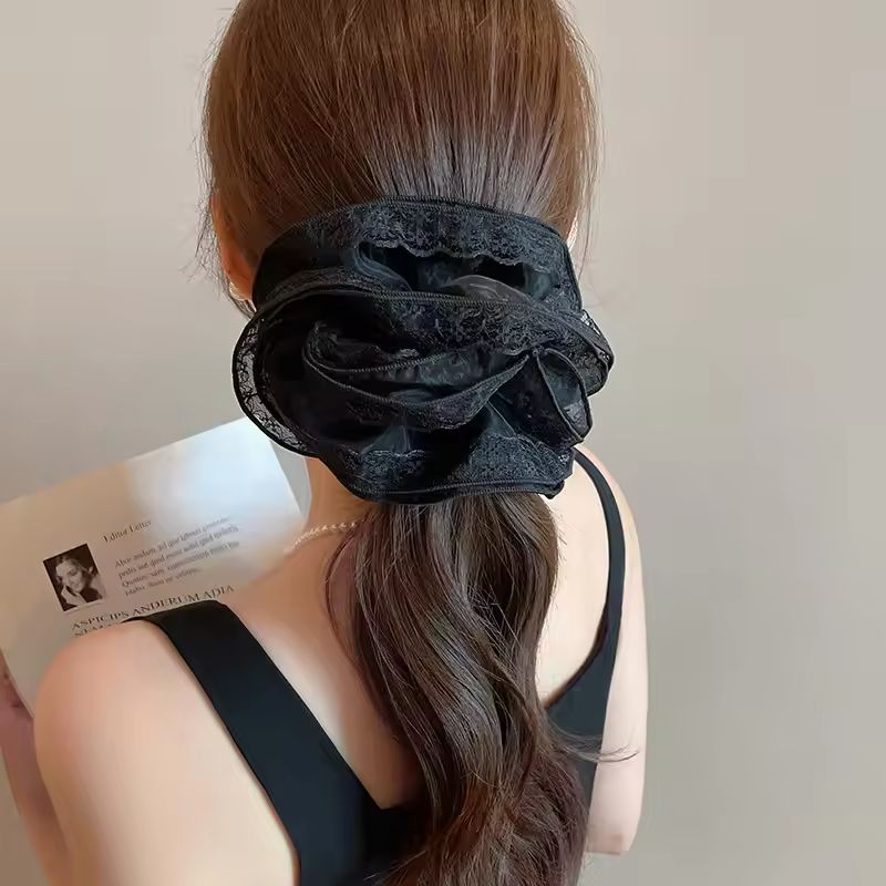 Person wearing a black lace scrunchie on their hair with a neutral background