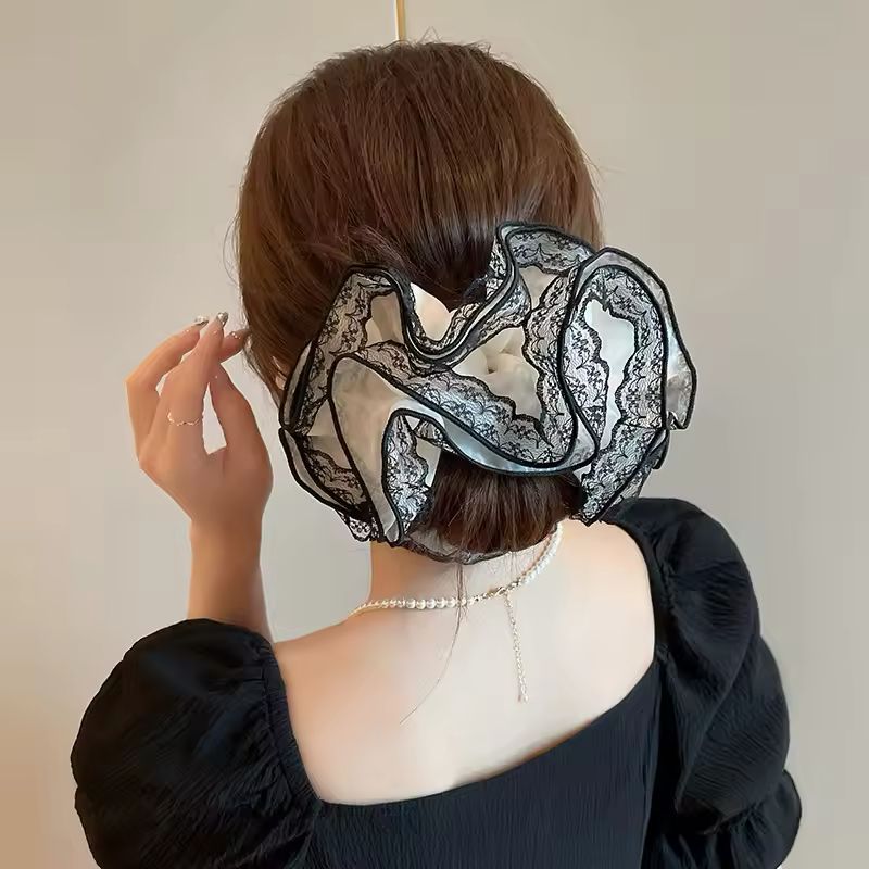 Person wearing a large black lace hair scrunchie accessory with a neutral background