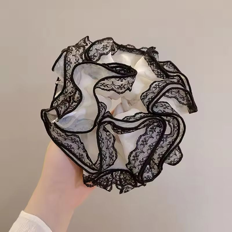 Black lace scrunchie held by a hand against a neutral background