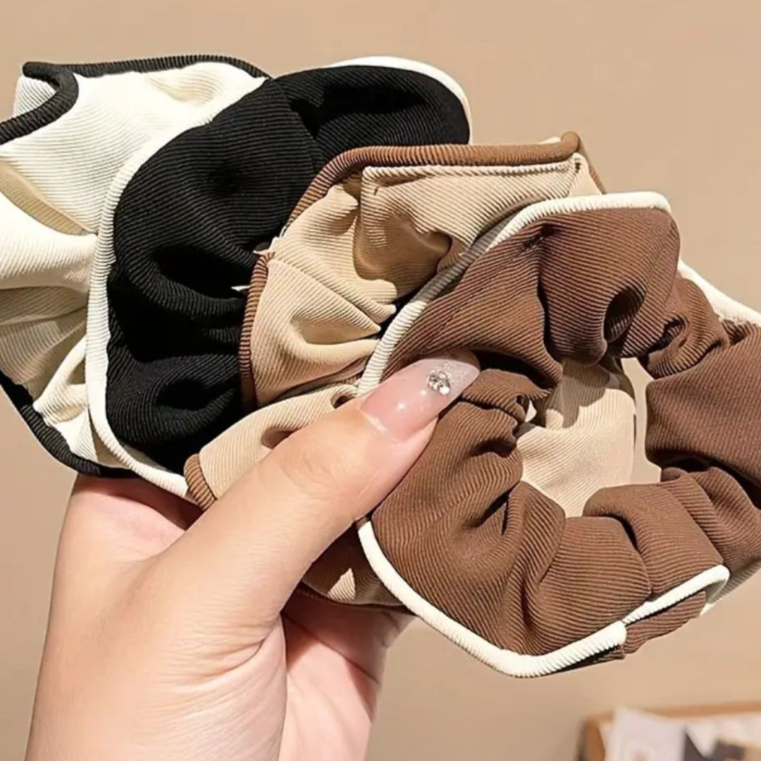 Set of three scrunchies in beige, black, and brown held by a hand against a beige background.