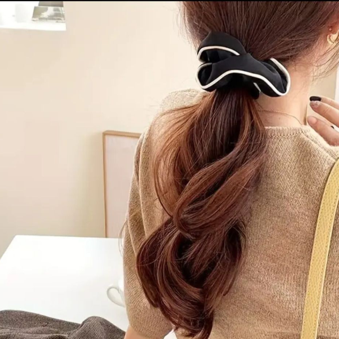 Person with a ponytail wearing a black hair tie, sitting on a bed.