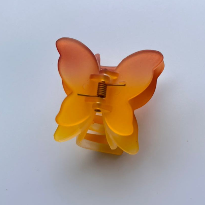 Butterfly-shaped hair clip with a gradient orange color on a white background