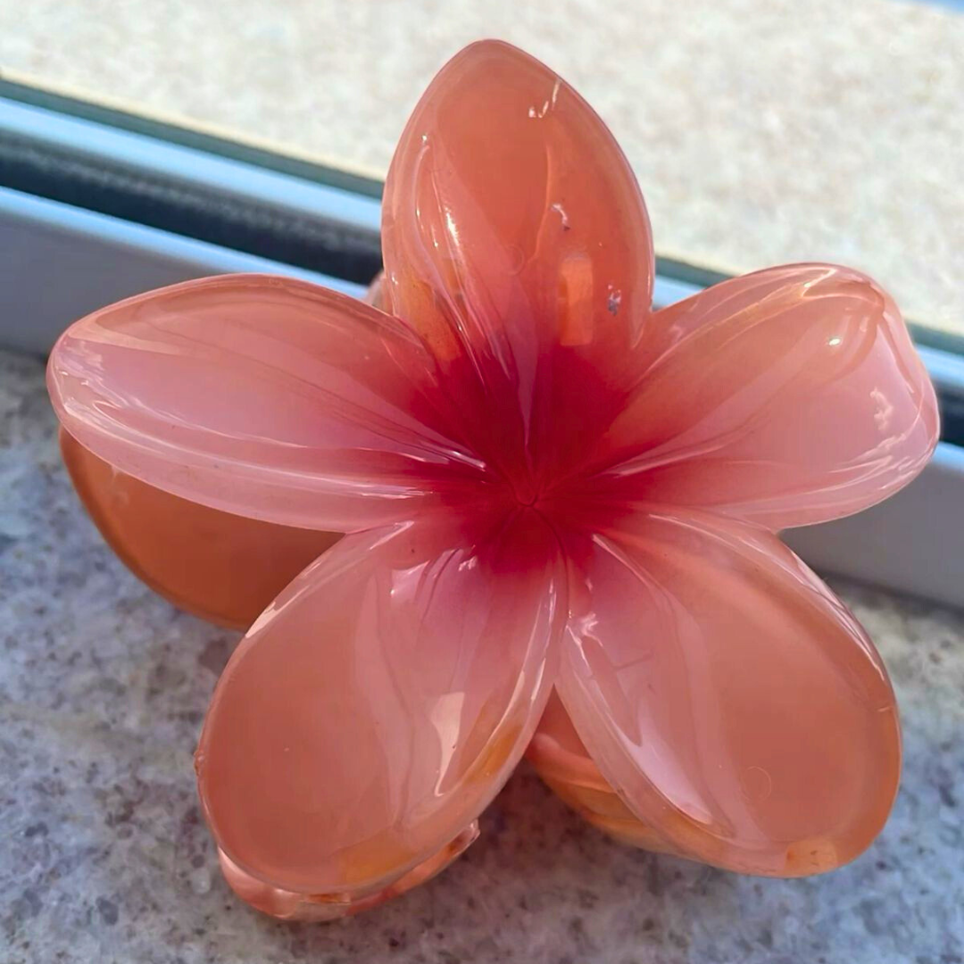 Flower-shaped hair clip with orange petals and red center on a textured surface