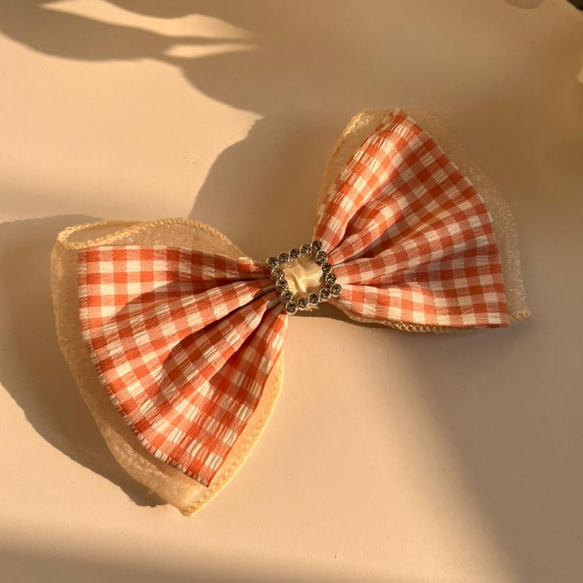 Checkered bow with a decorative center on a white surface with flowers in the background