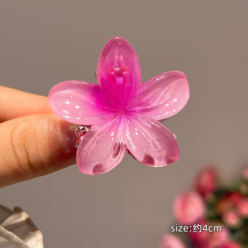 Pink flower-shaped hair clip held by a hand with a blurred background