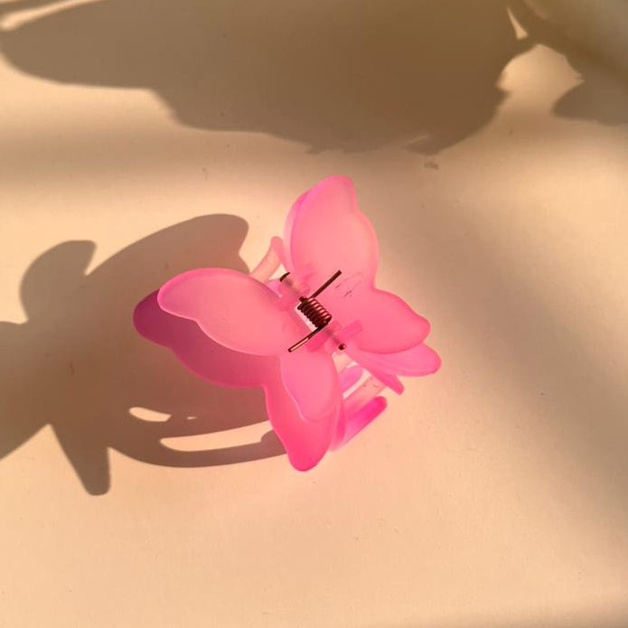 Pink butterfly-shaped hair clip on a light surface with shadows