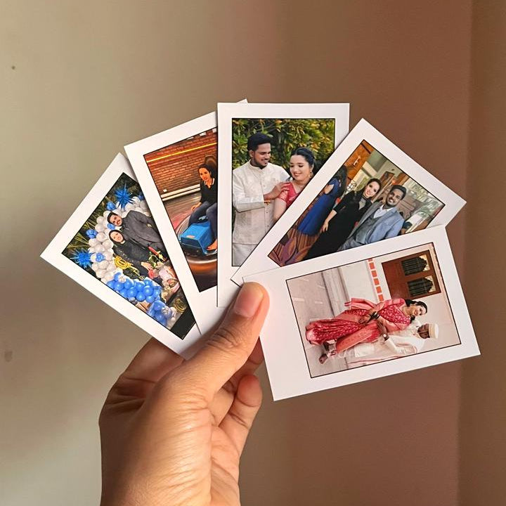 Hand holding a collection of small photo prints against a plain background